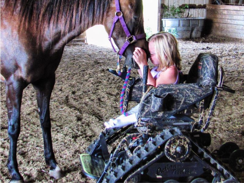 A young girl is petting her horse from her off-road Action Trackchair wheelchair.