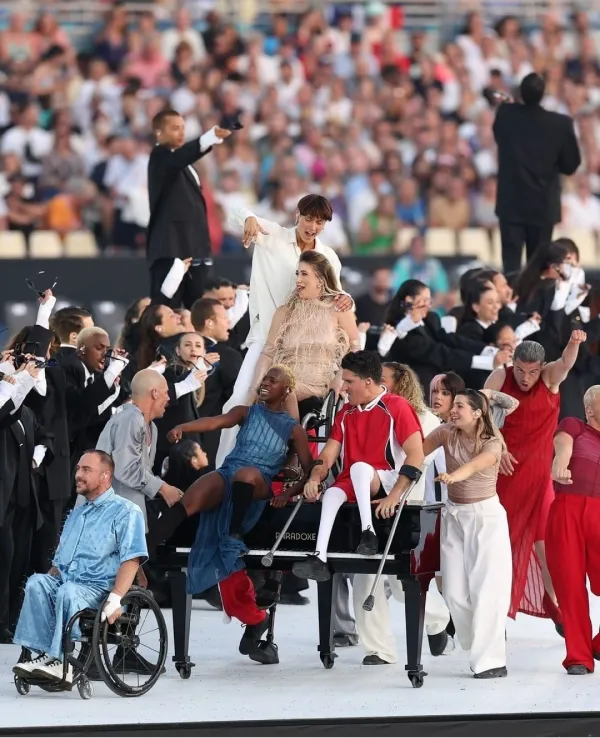 Alt text: Chelsie Hill is performing on top of a piano surrounded by dancers at the Opening Ceremony of the Paralympics.