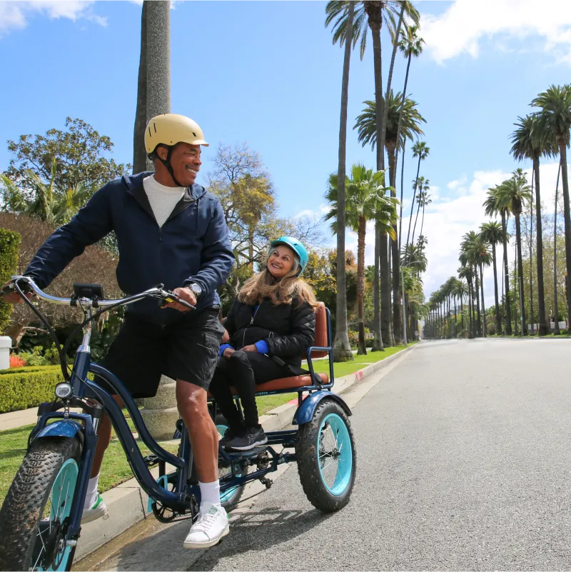 A man is riding a sixthreezeo Electric Tricycle Rickshaw with a smiling passenger in the back.