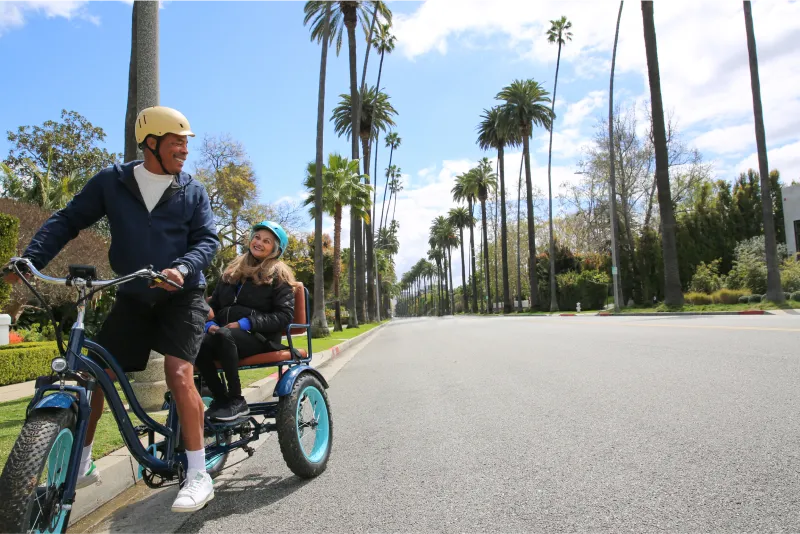 A man is riding a sixthreezeo Electric Tricycle Rickshaw with a smiling passenger in the back.