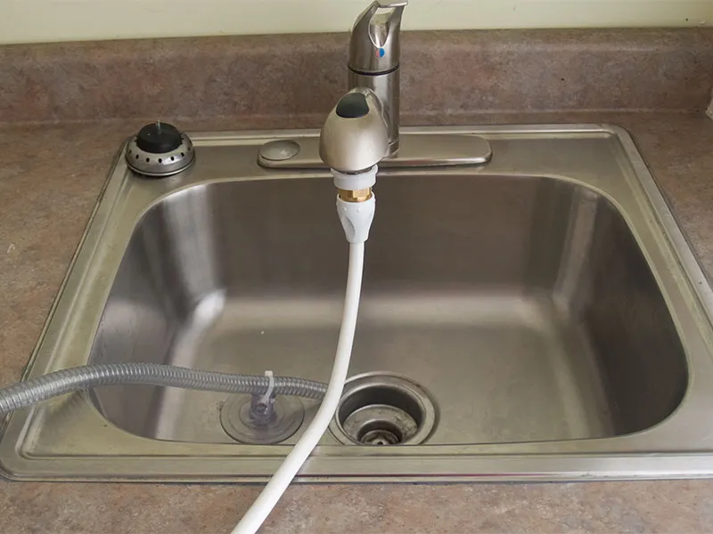 A sink with the FAWSsit Portable Shower tubing attached to the faucet.