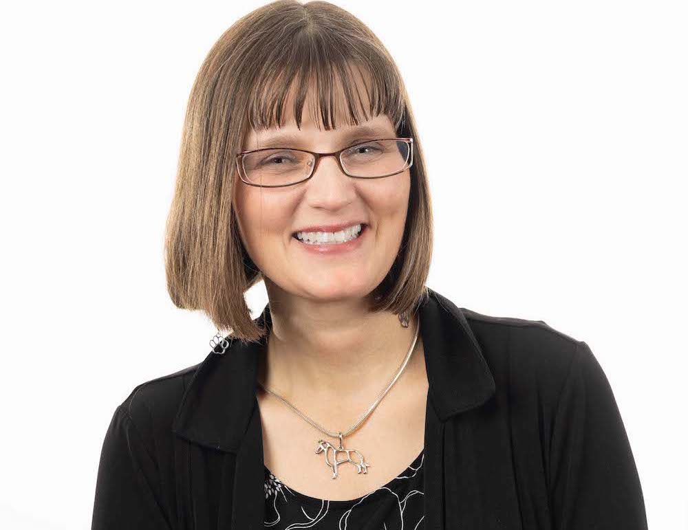 Kristin smiles at the camera, wearing a black top, black cardigan and dangly paw print earrings.