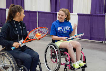 Racquets in hand, two wheelchair users pause their tennis game for a friendly chat.