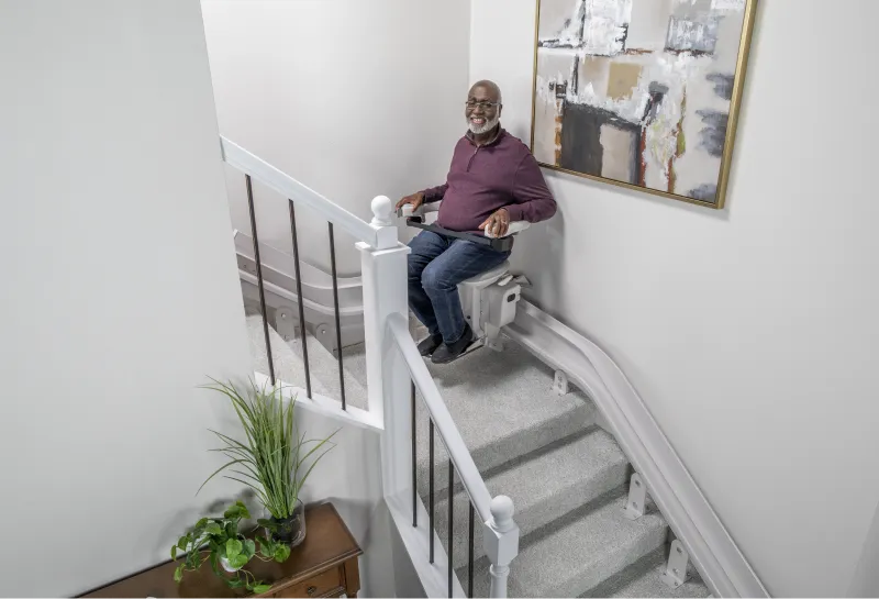 A smiling man is rounding his staircase landing on a curved Lifeway Mobility stair lift