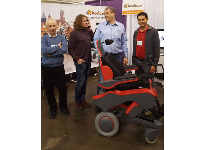 The CheelCare executive team, including co-founders Eugene Cherny –CEO, and Dima Paltsev –CFO. They stand in front of a Cheelcare banner and behind a red CheelCare Xceed power chair. Photo taken at the 2017 Abilities Expo in Toronto.