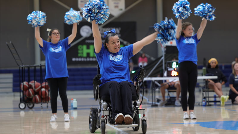 Woman in wheelchair cheers and dances with pompoms