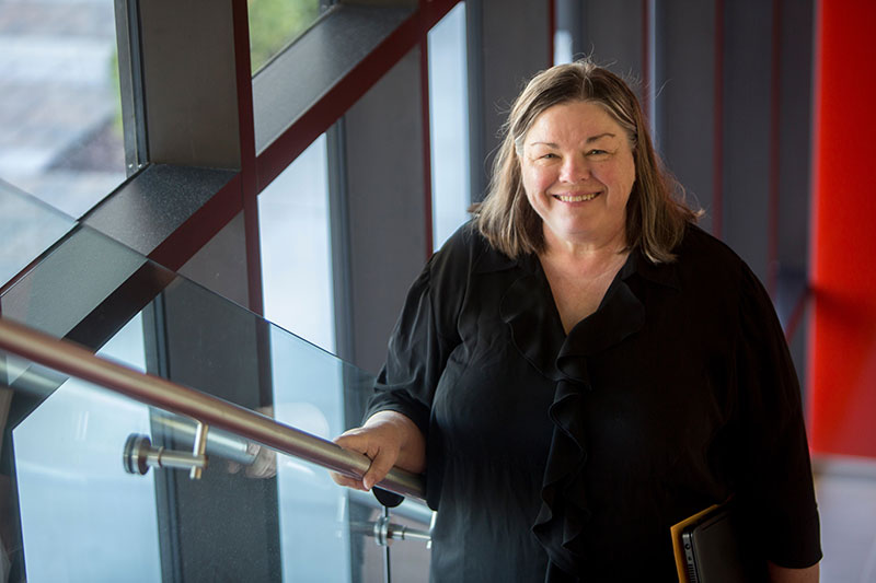 A smiling Nurse Linda in her loose-fitting black blouse pauses on the stairs to smile for the camera.