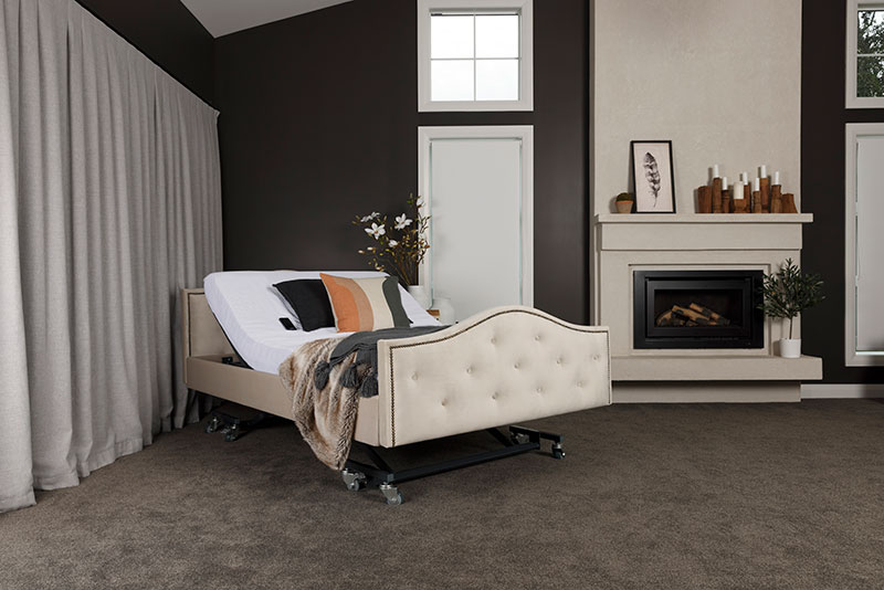 A full-sized homecare icare bed is inclined to a sitting position in a homey bedroom with a fireplace.