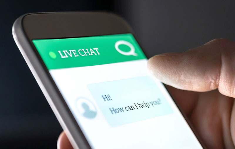 Close-up of a smartphone in a person’s hand that reads Live Chat and has the message: Hi! How can I help you?