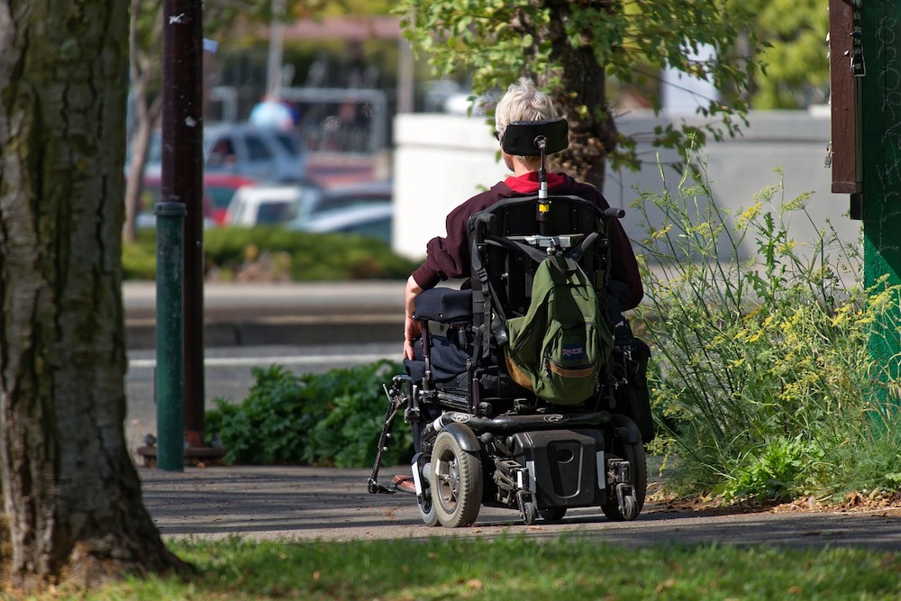 A woman is rolling away outside in a power wheelchair.