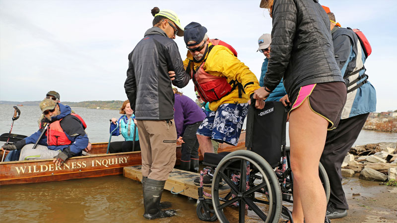 Picture of wheelchair user getting into boat with a group of people. 