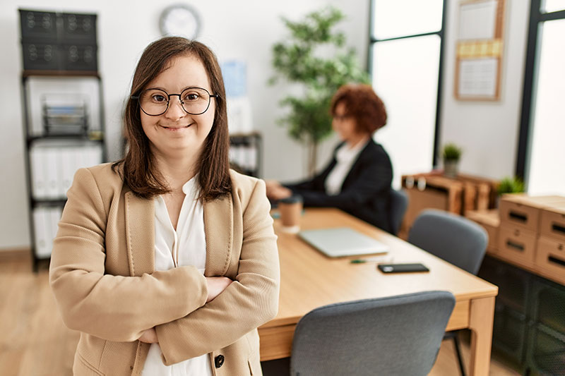 Woman in a workplace smiling at the camera while a colleage works in the background