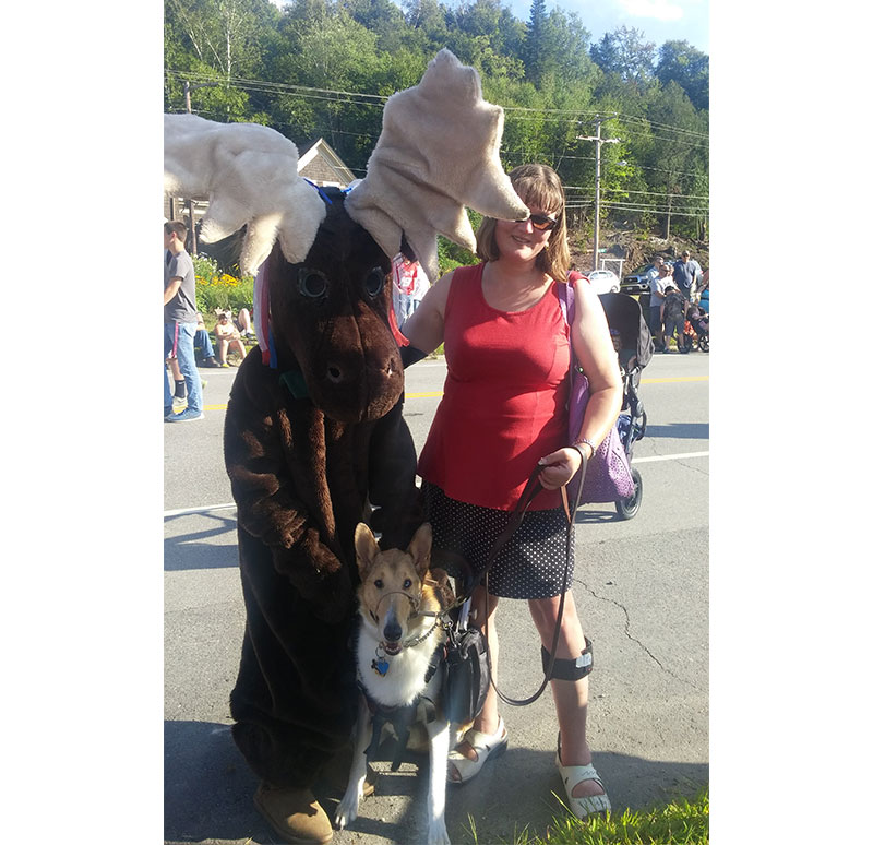 Kristin Hartness and her service dog, Asha, pose for the camera next to someone in a giant moose costume.