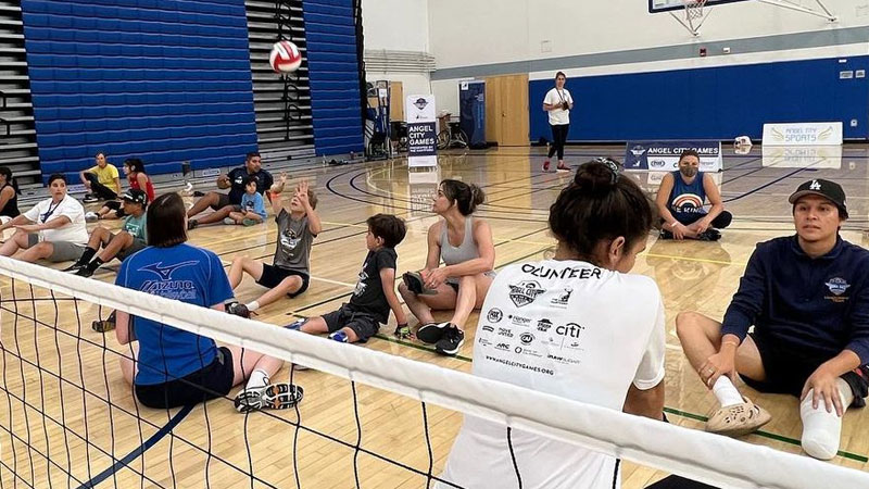 Join the fun with Angel City Sports as they put on a sitting volleyball demo! Pictured are several players of various abilities and ages sitting on the ground while playing the sport.