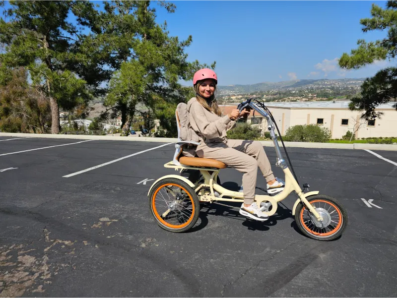 A woman is smiling as she rides the sixthreezero Simple Glide 500W Recumbent E Trike over a parking lot.