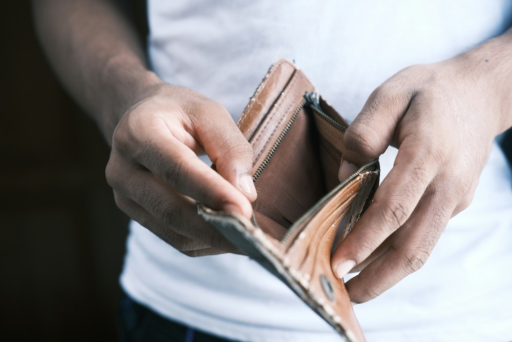 A man is opening a brown leather bifold wallet to reveal it empty.