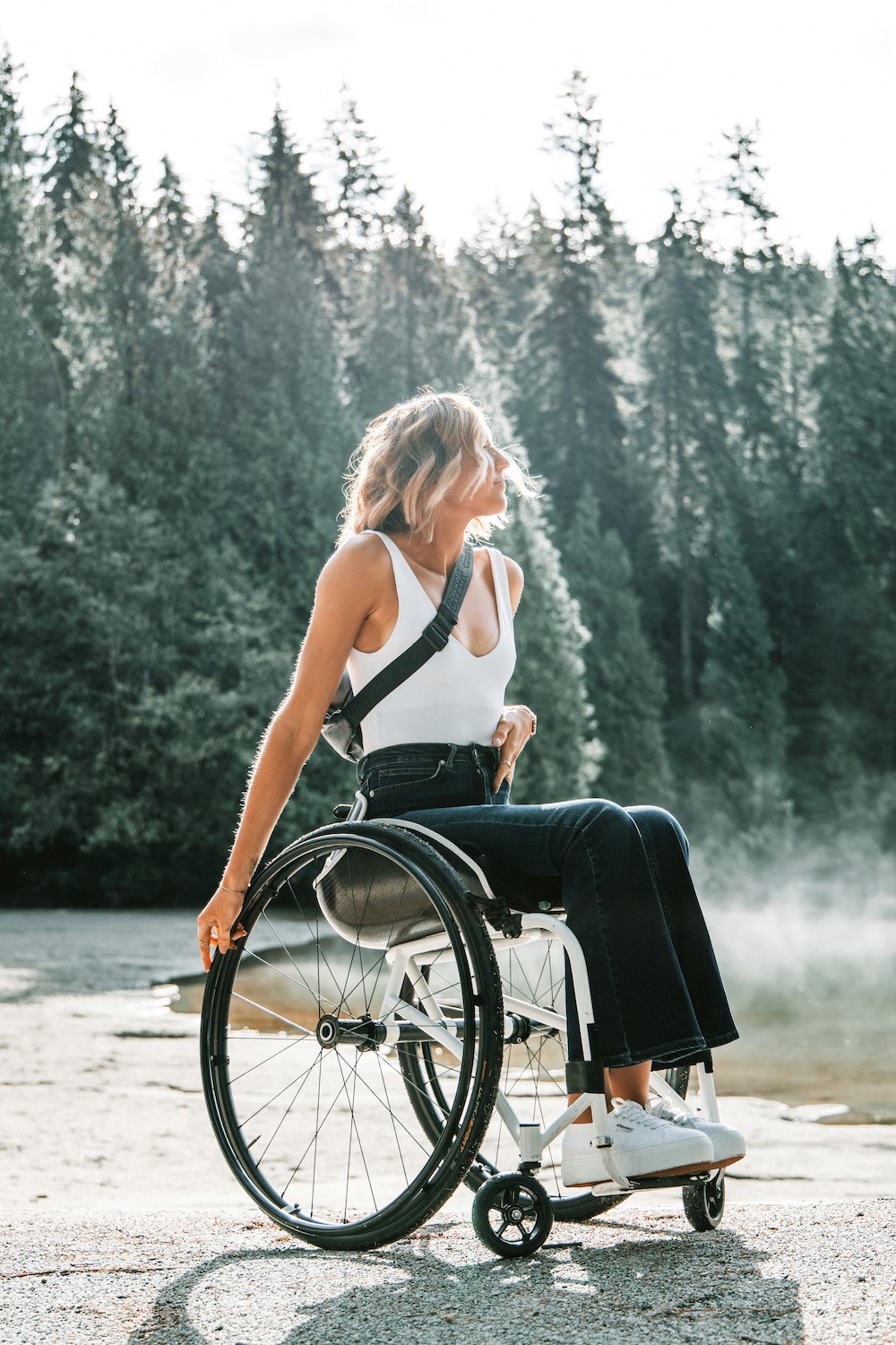 A woman in a wheelchair is looking off in the distance with a forest in the background.