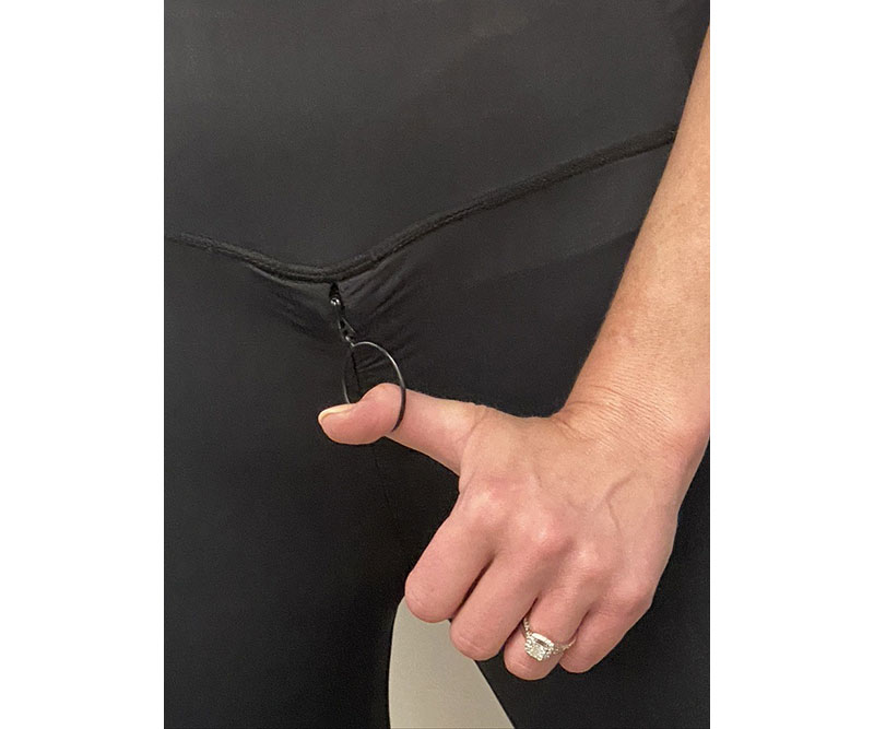 A woman’s thumb is hooked into the round, hollow, accessible zipper pull on a pair of Zip Hers tights.